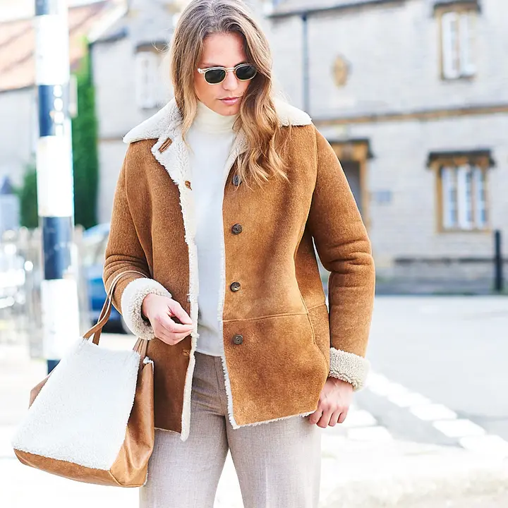Woman wearing an Owen Barry tan sheepskin coat with a shearling tote bag on a Somerset street